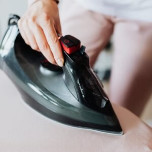 Close-up of a woman ironing clothes using a modern electric iron in a home setting.