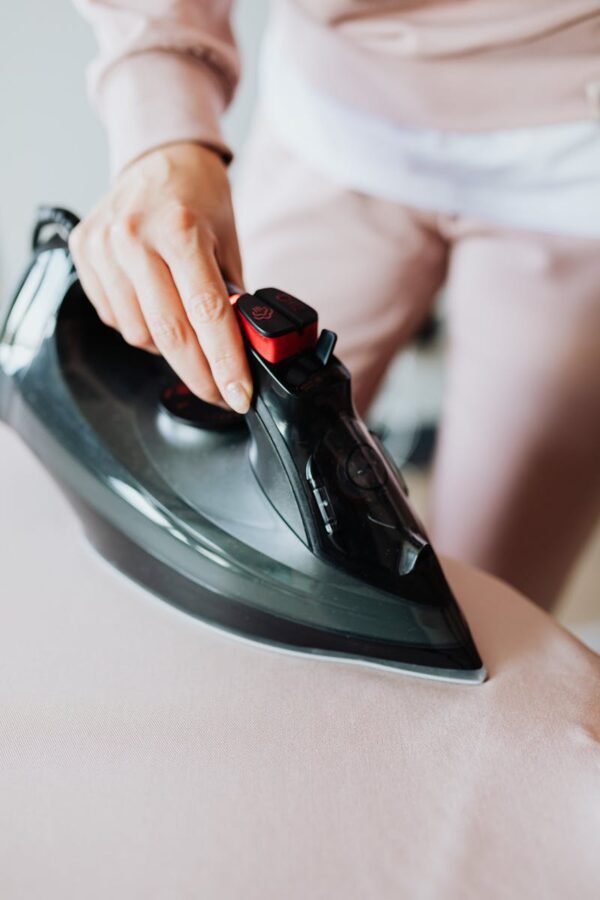 Close-up of a woman ironing clothes using a modern electric iron in a home setting.